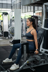 Fototapeta premium A sporty Asian woman in sportswear is exercising on a hip abduction, adduction machine in the gym.