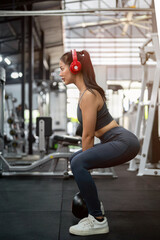 A sporty Asian woman is performing kettlebell squats at the gym, training her glute muscles.