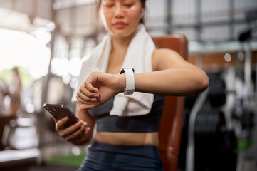 A sporty Asian woman in athletic wear is checking her workout results on her smartwatch at the gym.