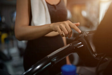A sporty woman in athletic wear adjusting her running program on a treadmill in a fitness gym.