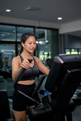 Fototapeta premium A sporty Asian woman in sportswear is running on an Elliptical cross trainer machine in a gym.