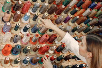 Woman tailor choosing colored spools of thread for sewing and embroidery