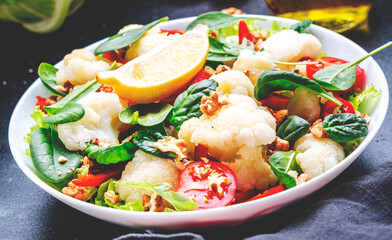 Autumn vegan salad with cauliflower and paprika, tomatoes, spinach with walnuts on gray background, top view