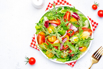 Vegan vegetable salad with tomatoes, cucumber, onion, lettuce and arugula. White background, top view