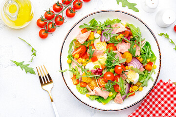 Tasty tuna vegetable salad with tomatoes, onion, corn, paprika, lettuce and arugula. White  background, top view