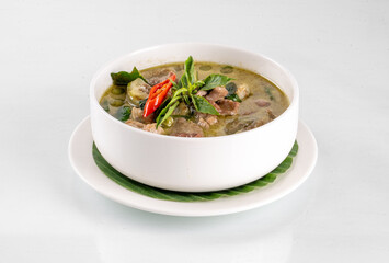 A bowl of delicious Thai green curry with fresh herbs and spices, presented on a white plate with a garnish of red chili peppers and leaves.