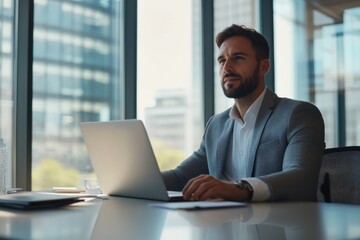 Fototapeta premium Confident Businessman Working On Laptop In Modern Office With City View