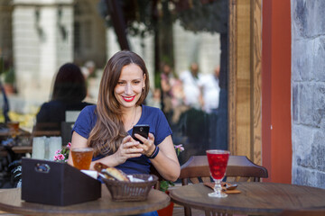 Young woman enjoying a drink while texting at an outdoor cafe in summer