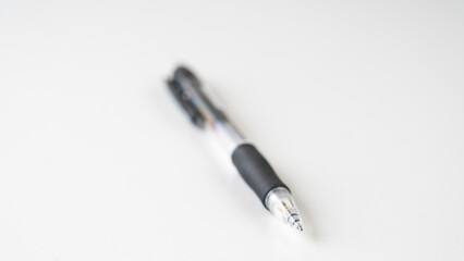 Fototapeta premium A black pen with a silver tip sits on a white surface. The pen is the only object in the image, and it is a ballpoint pen. Concept of simplicity and minimalism