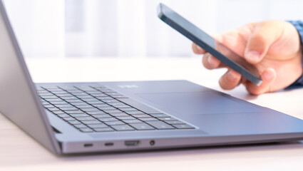 A person is using a laptop and a cell phone. Concept of multitasking and being connected to...