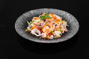 A delicious plate of fresh seafood salad with various vegetables, elegantly presented on a textured round plate, against a black background.