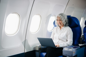  Asian seniorexecutive excels in first class, multitasking with digital tablet, laptop and...