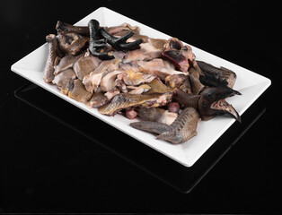 A plate of assorted raw poultry pieces on a white rectangular dish against a black background, ready for cooking or culinary preparation.
