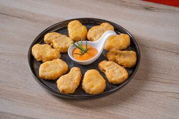 A plate of delicious chicken nuggets arranged around a dip bowl with sauce and garnished with a sprig of rosemary on a wooden table.