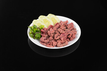 A plate of finely chopped cooked meat paired with sliced cucumbers and fresh herbs, presented on a black background.