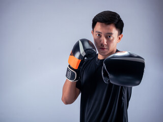 An Asian man in a serious boxing stance throws a punch while wearing black and orange boxing...
