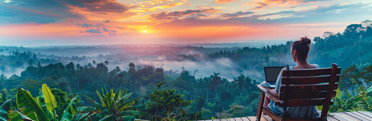 young freelancer woman working at the computer at sunset or sunrise on the top of the mountain