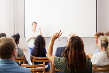 Businesswoman with hand raised sitting behind colleagues during meeting in office
