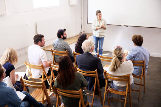 High angle view of smiling businesswoman giving presentation to coworkers against blank projection screen at office