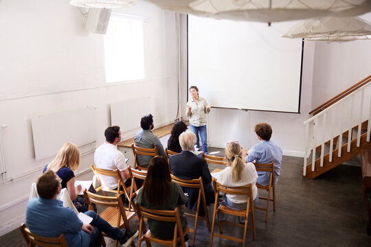 High angle view of businesswoman giving presentation to colleagues against blank projection screen at office