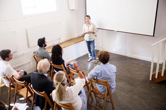 High angle view of businesswoman giving presentation to coworkers against blank projection screen at office