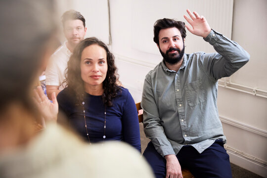 Businessman with hands raised sitting by colleagues in office during presentation