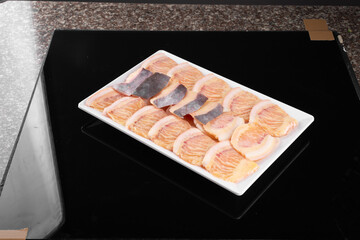 A tray of fresh fish fillets neatly arranged on a black surface, ready for cooking or serving in...