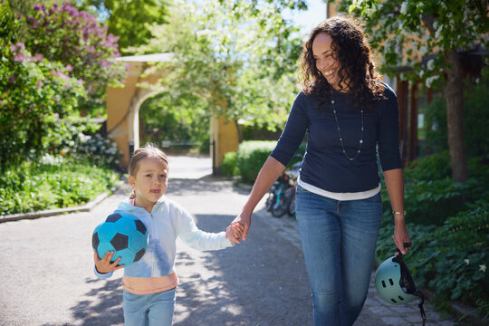 Cheerful mother looking at daughter while walking on footpath in parks