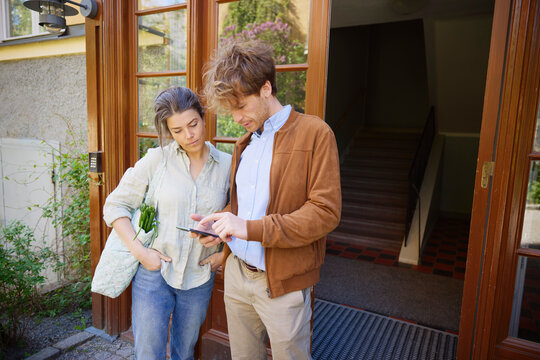 Mid adult couple using mobile phone against building entrance