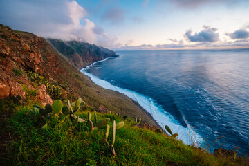 View of rough ocean with waves, volcanic beach, sunset over a huge cliff  in Lighthouse Ponta do Pargo, Madeira, Portugal