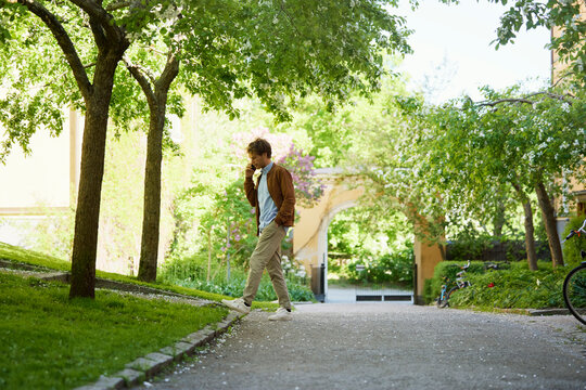 Full length side view of man talking through smart phone on footpath amidst trees