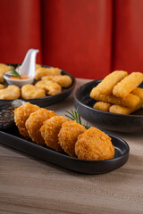 A variety of fried appetizers, including chicken nuggets, mozzarella sticks, and potato croquettes, elegantly arranged on black plates.