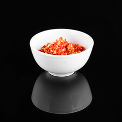 A white bowl filled with finely chopped red peppers, isolated on a black background, showcasing a vibrant and appetizing presentation.