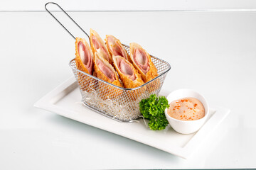 Appetizing fried ham and cheese roll-ups served with dipping sauce and garnished with fresh...