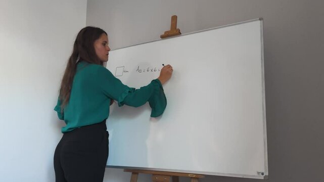 Girl teaching math on a whiteboard indoors, professionally dressed writing equations for area of square