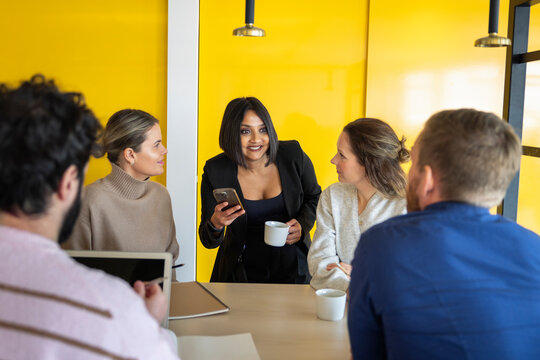 Smiling businesswoman holding mobile phone while discussing ideas with colleagues in office