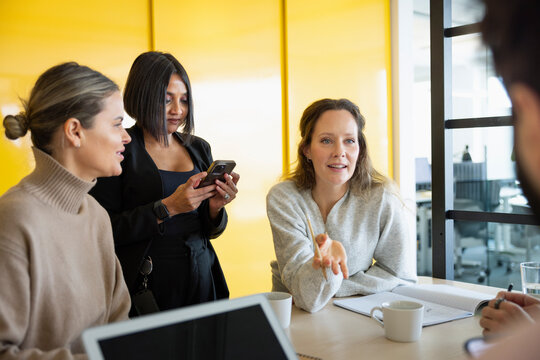 Businesswoman using phone while colleagues discussing over table in office
