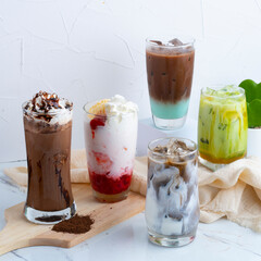 Assorted iced beverages, including coffee, latte, and fruity drinks, served in clear glasses with whipped cream and toppings.