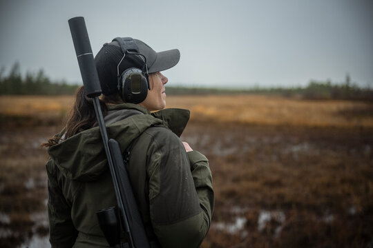 Rear view of female hunter carrying gun while wearing headphones in forest