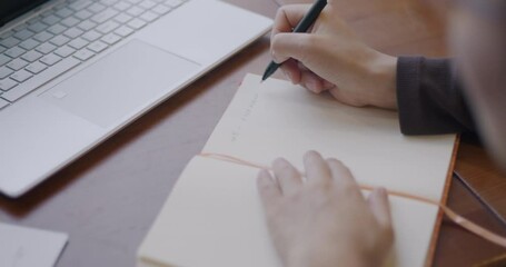 Close-up of female hand writing in notebook while businesswoman working at table in office. Finance and business planning concept.