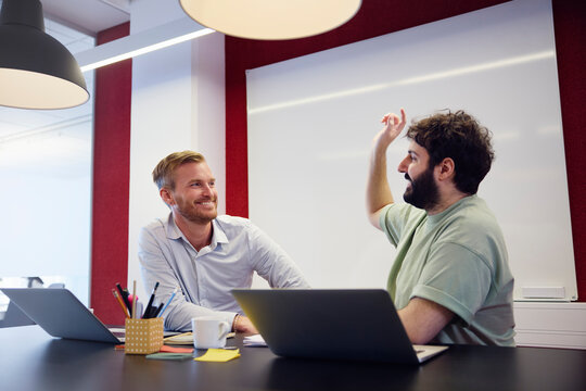 Smiling corporate colleagues talking while sitting over table in office
