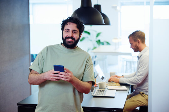 Portrait of businessman using phone while colleague working over table in office