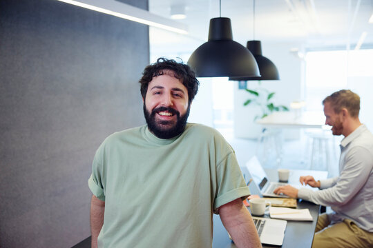 Portrait of smiling young businessman standing while colleague working over table in office