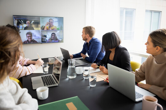 Male and female business colleagues doing virtual meet with team sitting in meeting room