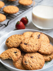 A plate of freshly baked oatmeal raisin cookies garnished with a strawberry, accompanied by a glass of milk and scattered blueberries, set against a light, natural background for a cozy snack scene.