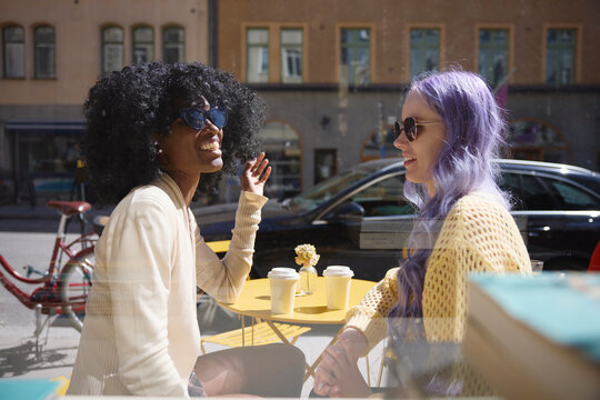 Young female friends sitting at cafe seen through glass window