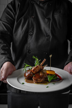 Chef presenting a gourmet dish of lamb chops with vegetables, elegantly plated on a white dish, showcasing fine dining cuisine.