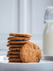 A stack of freshly baked oatmeal raisin cookies neatly arranged on a white plate, with a bottle of milk in the background. The scene is set in a bright kitchen, creating a cozy snack moment.