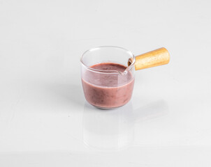 Close-up of a glass cup with a wooden handle, filled with berry smoothie, isolated on a white background.