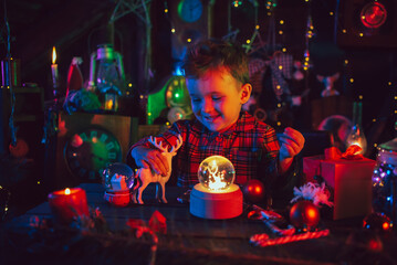 A fabulous, magical, Christmas atmosphere. A little boy, Santa's assistant, is sitting at a table in Christmas decorations. Postcard. colored light